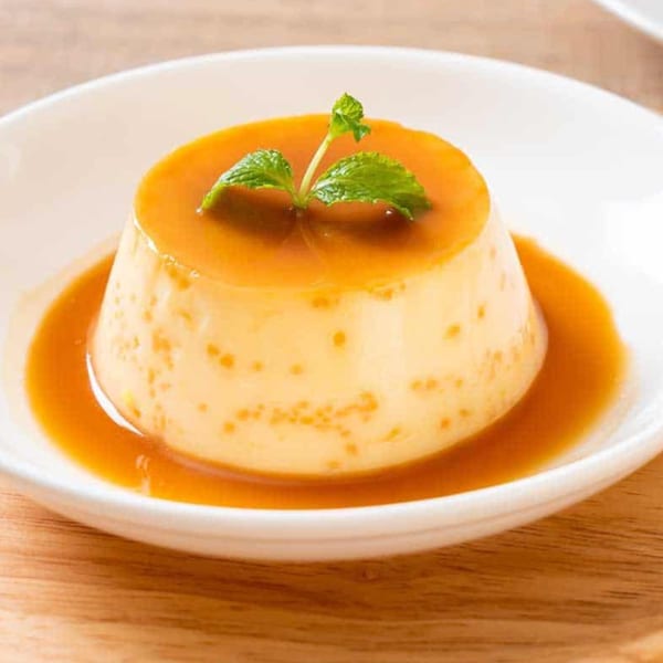 Cuban flan dessert with caramel sauce and a mint garnish in a white bowl.