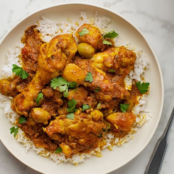 A bowl of Cuban chicken fricassee with potatoes, olives, and cilantro over white rice.