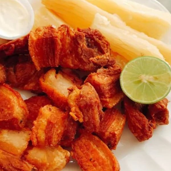 Crispy fried pork chunks, yuca fries, a lime wedge, and a side of white dipping sauce.